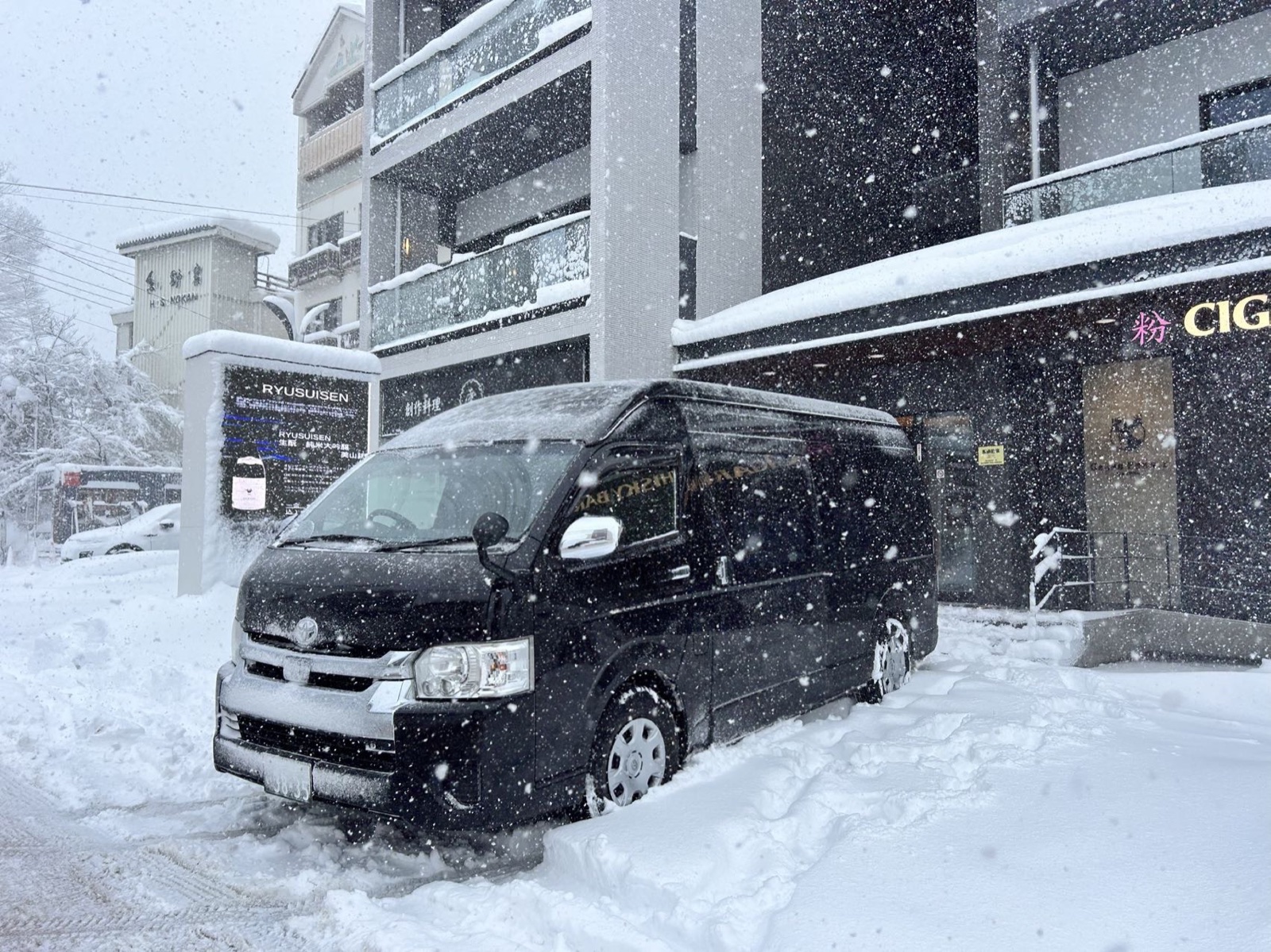 Private minibus collecting guests at a Hakuba hotel during snowfall